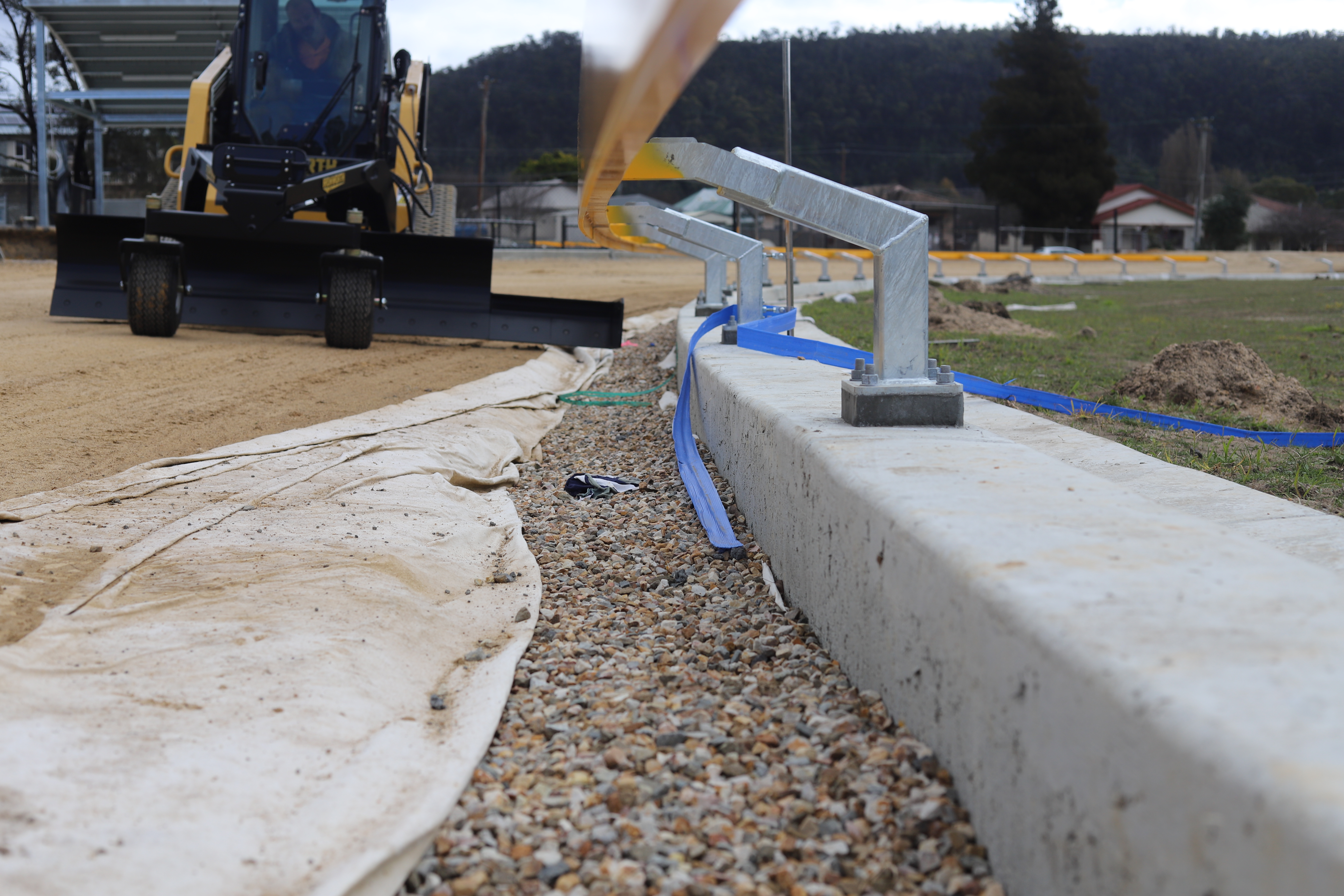 Ironworth grader working beside a gravel drainage channel and concrete edge